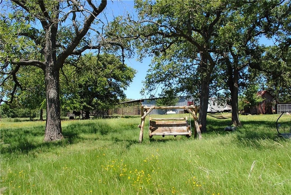 21741 East Interstate 10 Luling, TX 78648 - Photo 3 of 11 A rustic wooden swing offers a tranquil spot amidst mature trees and a grassy field.