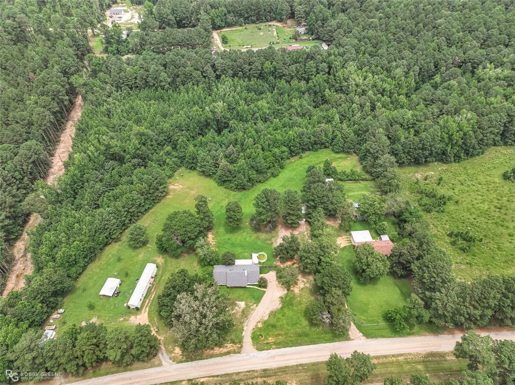 1426 Caney Lake Road Minden, LA 71055 - Photo 32 of 36 Expansive rural property featuring a primary residence with a dark gray roof, two ancillary structures, a gravel driveway, and surrounding green spaces with mature trees and dense woodland