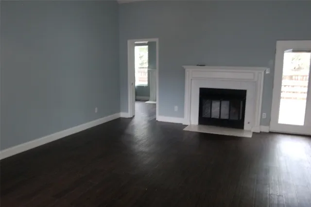 an empty room with wooden floor fireplace and windows