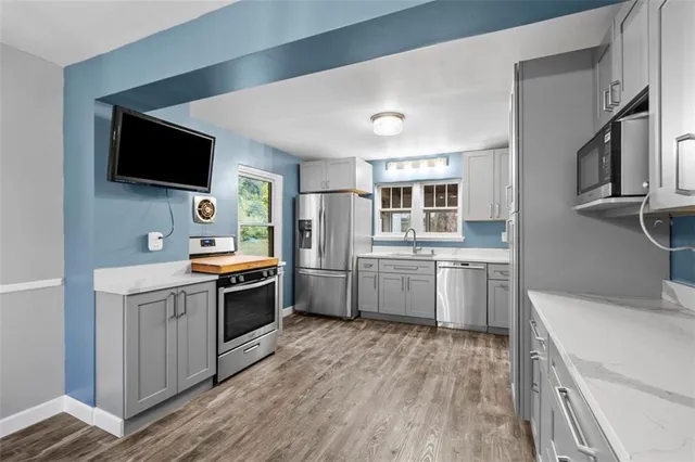 a kitchen with stainless steel appliances a stove top oven a sink dishwasher a refrigerator and white cabinets with wooden floor