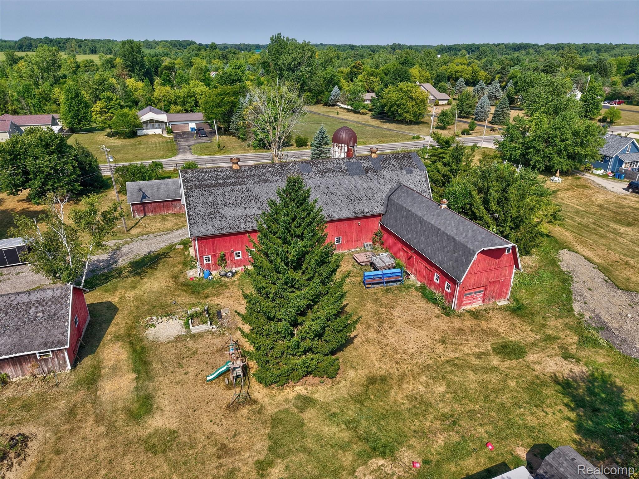 1175 South Morrish Road Flint, MI 48532 - Photo 61 of 72 Expansive property featuring multiple red barn structures with dark shingle roofing, a large evergreen tree, and a rural setting surrounded by mature deciduous and coniferous trees