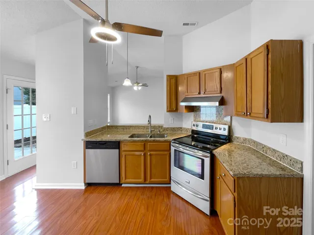 a kitchen with stainless steel appliances granite countertop wooden cabinets a stove a sink and a wooden floor