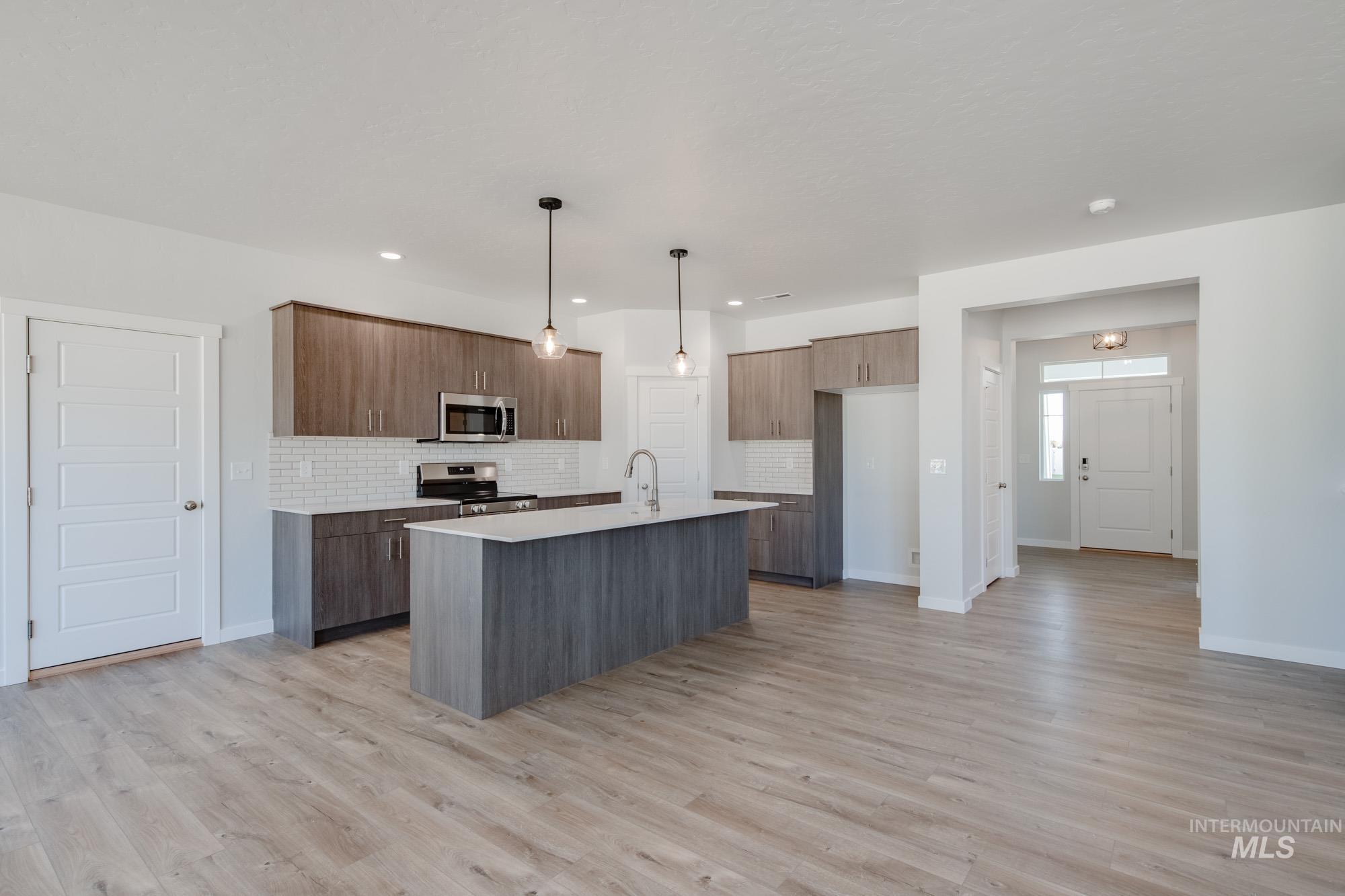 5304 Castleton Avenue Nampa, ID 83686 - Photo 10 of 25 Kitchen featuring tasteful backsplash, hanging light fixtures, light wood-style floors, a center island with sink, and appliances with stainless steel finishes