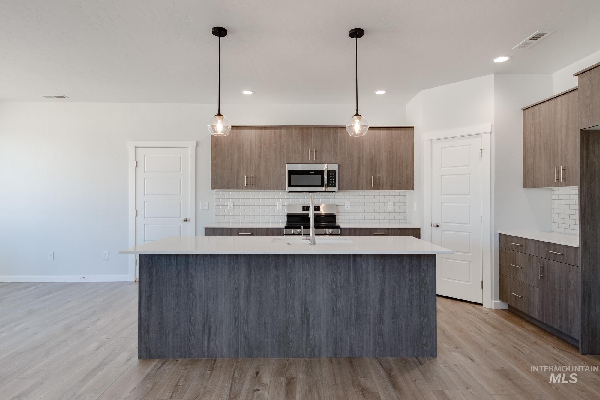 5304 Castleton Avenue Nampa, ID 83686 - Photo 3 of 25 Kitchen featuring backsplash, a kitchen island with sink, decorative light fixtures, modern cabinets, and light wood-style floors