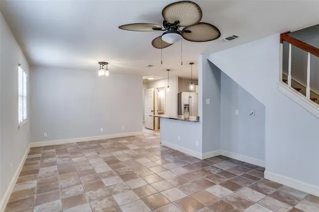 a view of an empty room with a chandelier fan and kitchen view