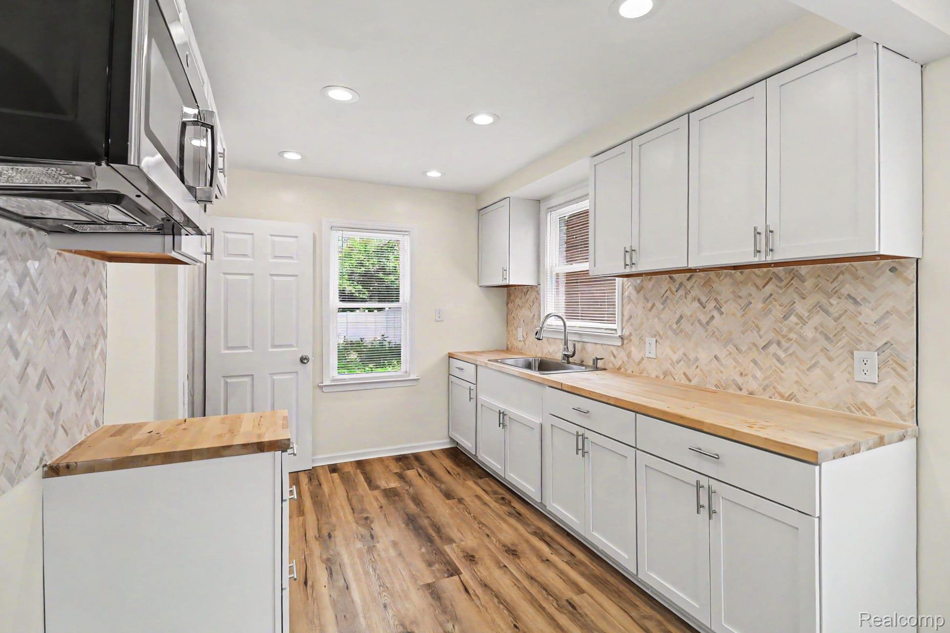 16682 Robson Street Detroit, MI 48235 - Photo 10 of 19 Kitchen featuring wood-finish flooring, white cabinetry, light wood countertops, and a herringbone-patterned tile backsplash