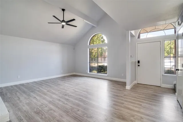 an empty room with wooden floor a ceiling fan and windows