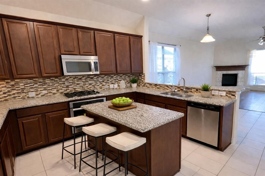 620 Calliopsis Street Little Elm, TX 75068 - Photo 4 of 30 Updated kitchen featuring granite countertops, maple wood cabinetry, stainless steel appliances, stylish mosaic backsplash, and a center island overlooking the spacious living area.