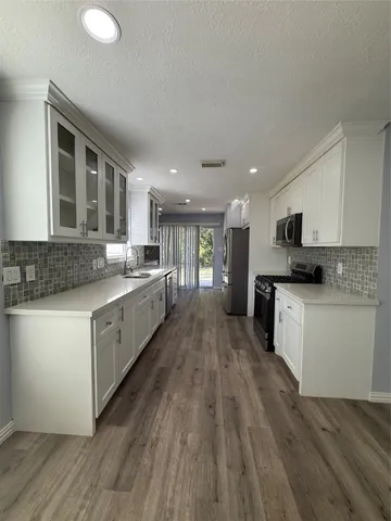 a large kitchen with stainless steel appliances granite countertop a stove a sink and white cabinets