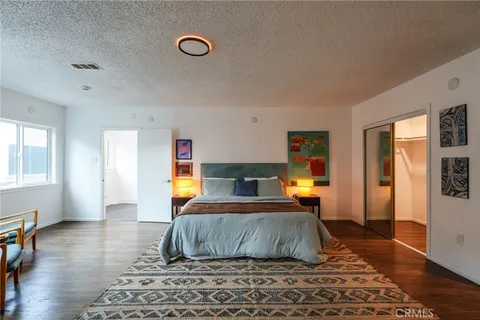a bedroom with a bed a mirror on dresser and a wooden floor