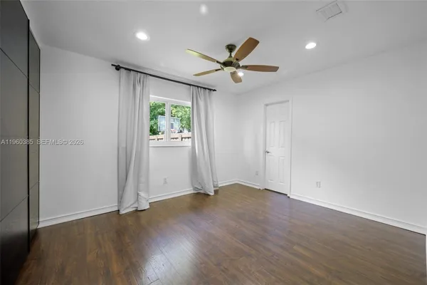 an empty room with wooden floor fan and windows