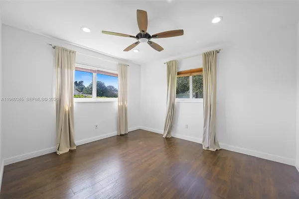 an empty room with wooden floor ceiling fan and windows