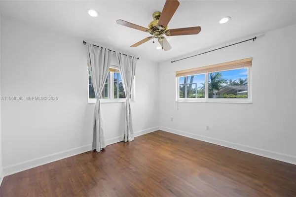 an empty room with wooden floor ceiling fan and windows