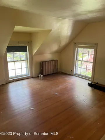 an empty room with wooden floor and windows with curtains
