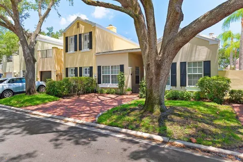 a view of a brick house with a yard plants and large tree