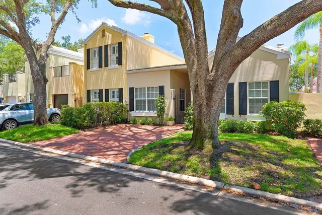 a view of a brick house with a yard plants and large tree