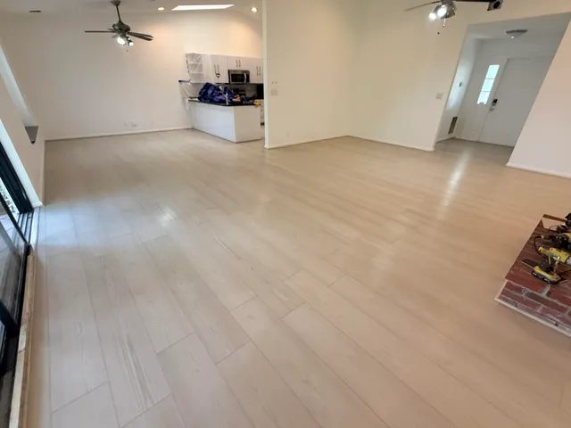 an empty room with wooden floor and a way to kitchen