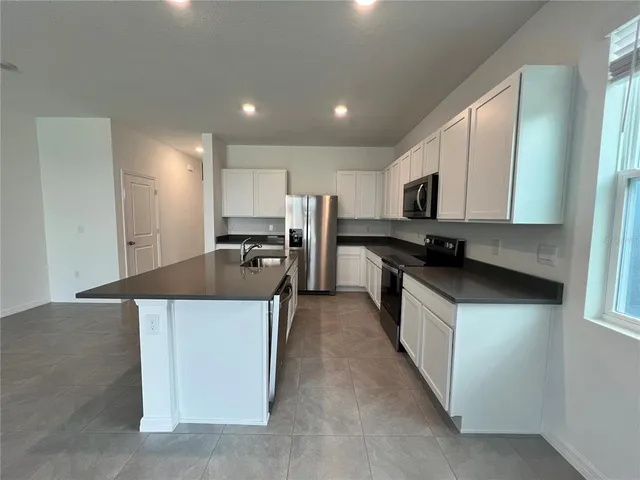 a kitchen with stainless steel appliances granite countertop a stove top oven a sink a refrigerator white cabinets and wooden floor