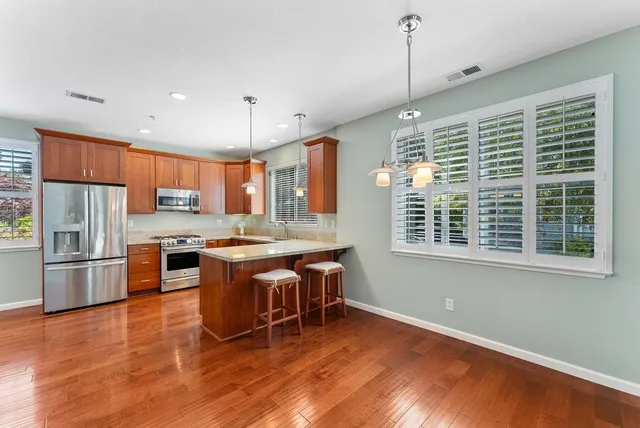 a kitchen with stainless steel appliances granite countertop a refrigerator a sink dishwasher a stove and a dining table with wooden floor