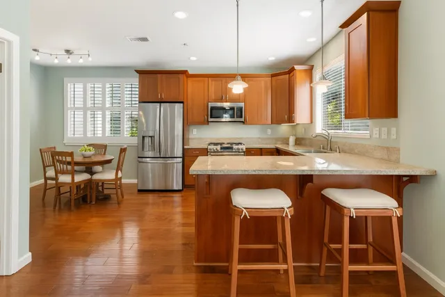 a kitchen with stainless steel appliances granite countertop a table chairs sink and wooden cabinets