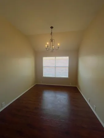 an empty room with wooden floor chandelier and windows
