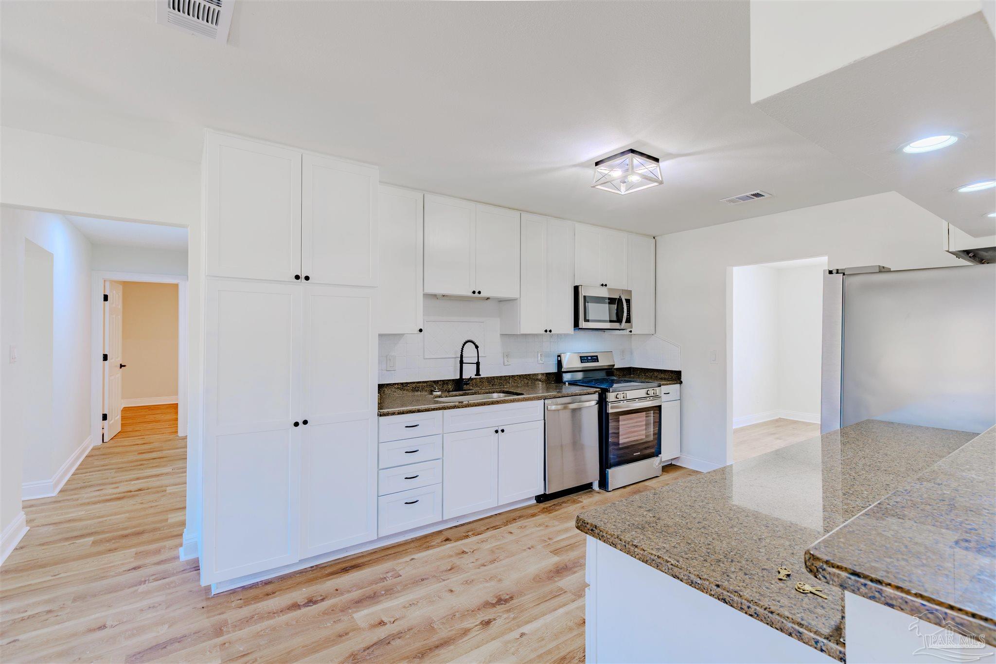 2115 Stallion Road Cantonment, FL 32533 - Photo 19 of 70 a large kitchen with granite countertop a stove top oven a sink dishwasher and a refrigerator with wooden floor