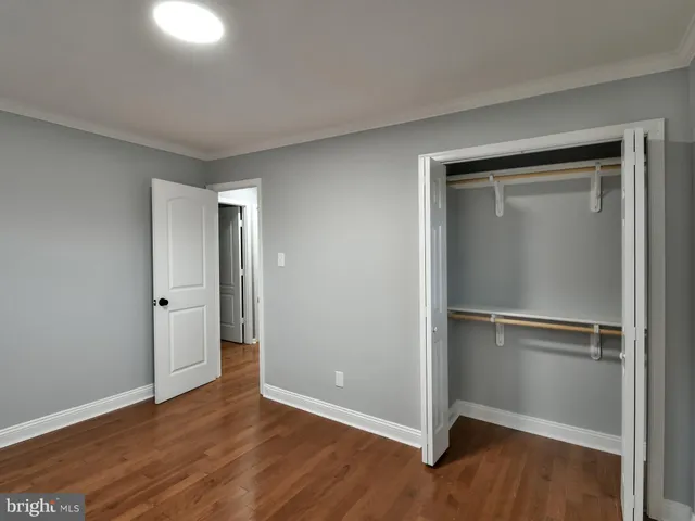 a view of an empty room with wooden floor & a window