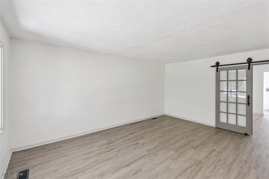 3930 Wood Road Madison, OH 44057 - Photo 7 of 45 Unfurnished room with a barn door, light wood-style flooring, and a textured ceiling