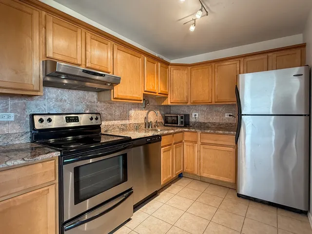 a kitchen with granite countertop a refrigerator stove top oven and cabinets