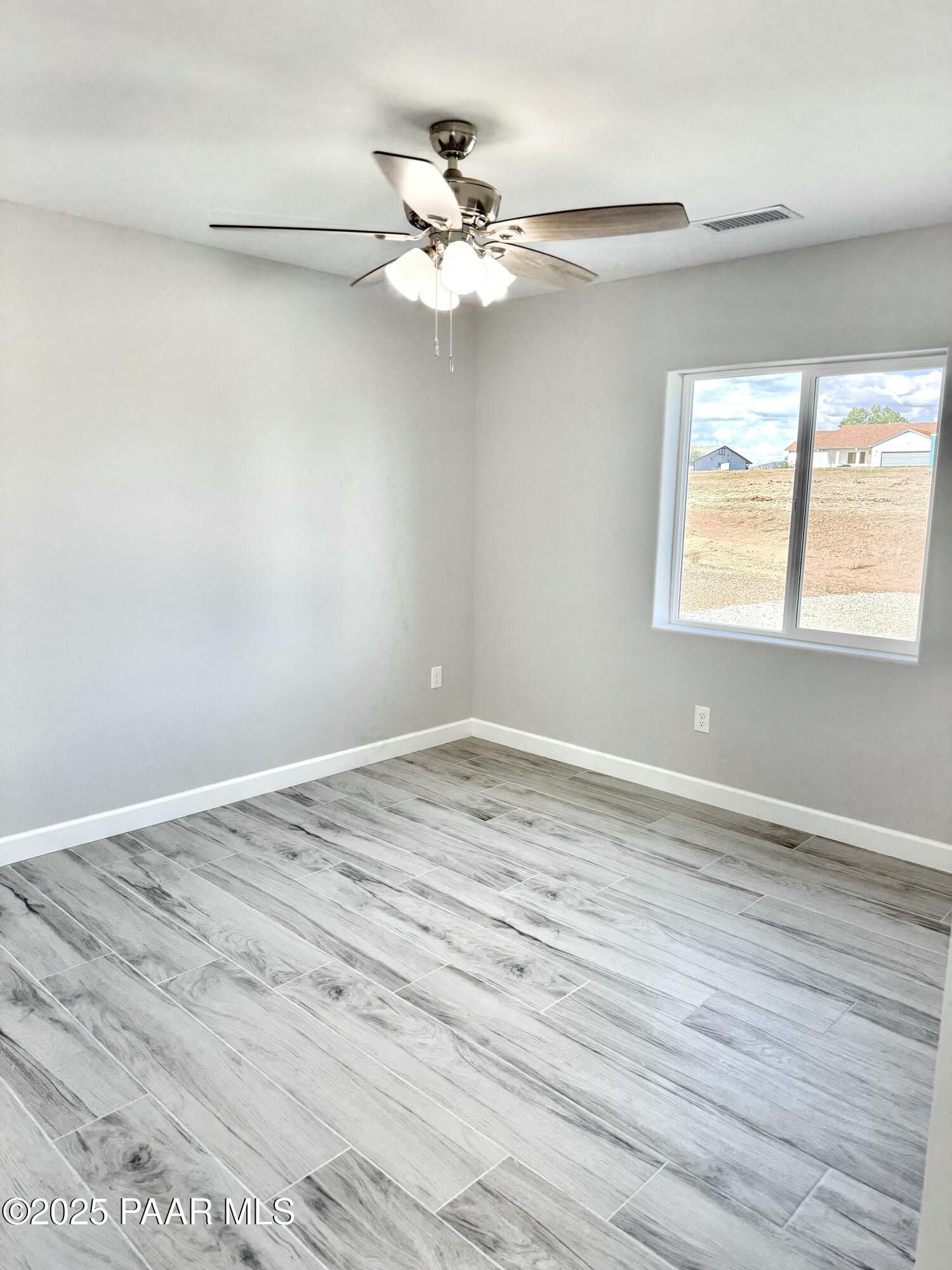 20182 East Mesa Verde Road Mayer, AZ 86333 - Photo 9 of 17 an empty room with wooden floor chandelier fan and windows