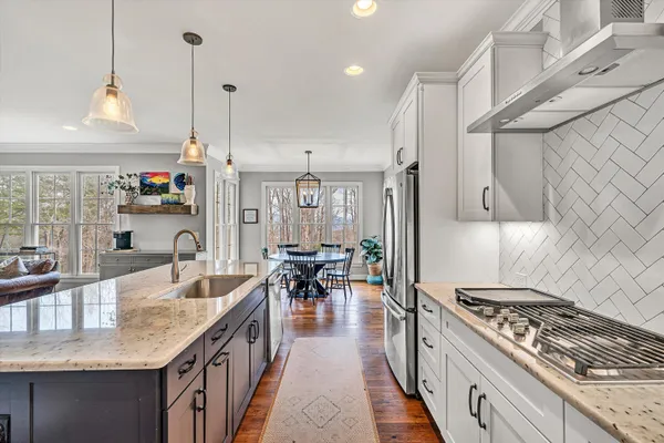 a kitchen with stainless steel appliances granite countertop a stove a sink dishwasher oven a dining table and chairs with wooden floor