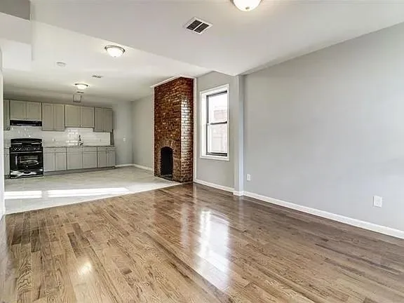 a view of empty room with wooden floor and kitchen view
