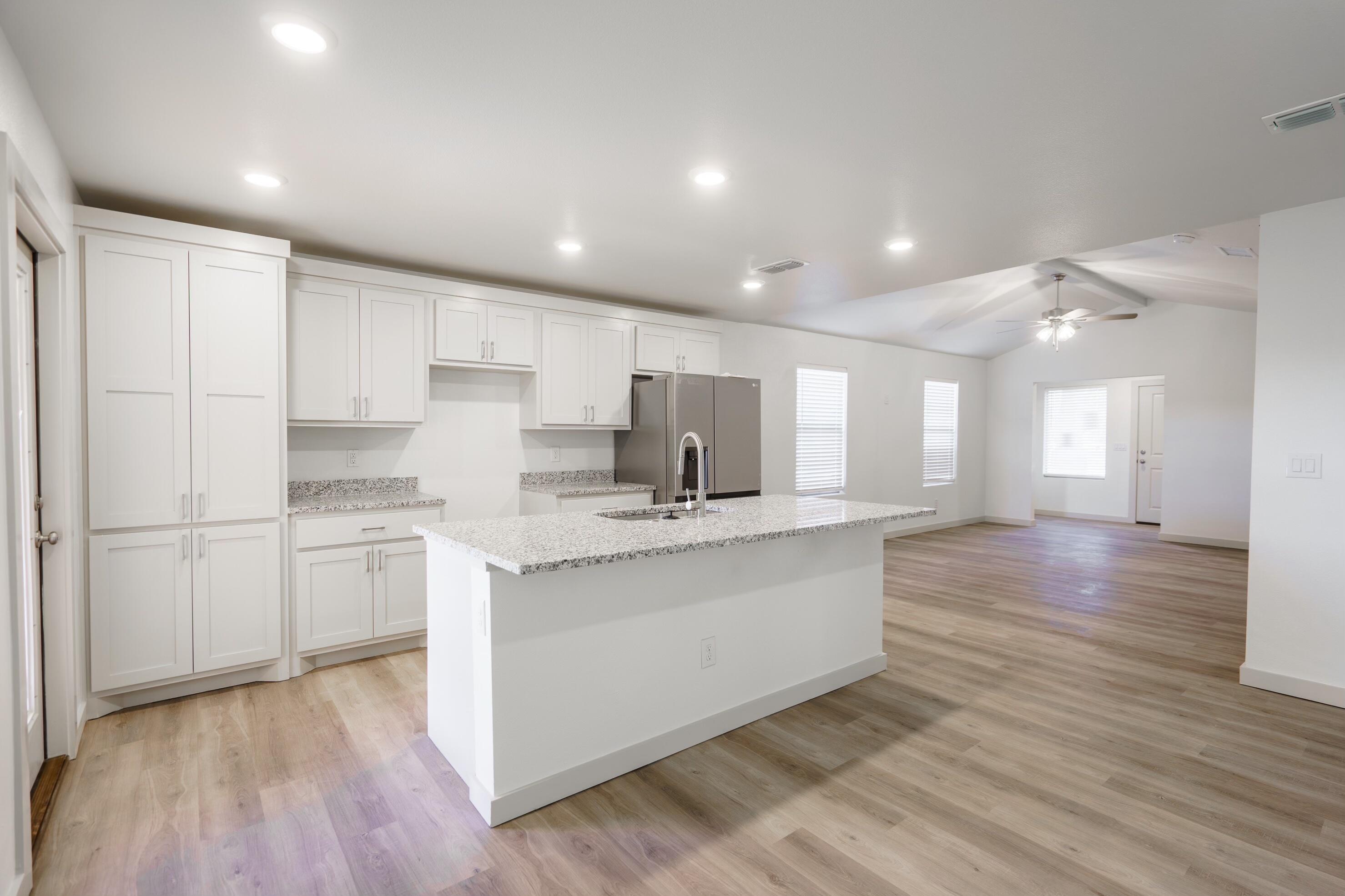 a kitchen with stainless steel appliances granite countertop a sink a stove a refrigerator and white cabinets with wooden floor