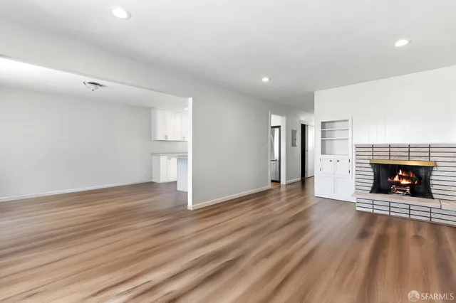 a view of an empty room with wooden floor fireplace and a window