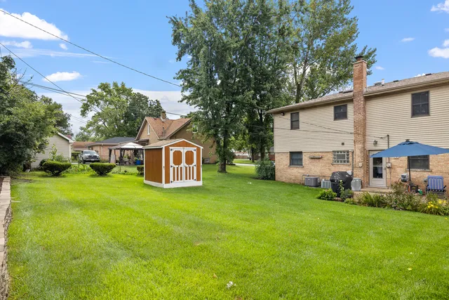 a view of a yard in front of a house with plants and large tree