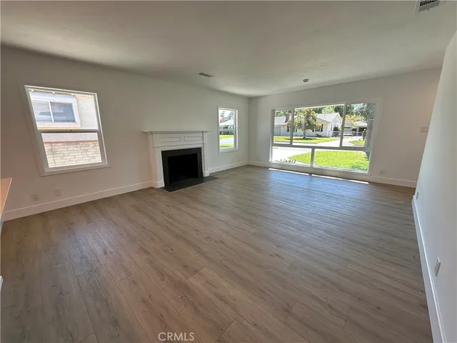 an empty room with wooden floor fireplace and windows
