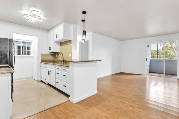 a kitchen with granite countertop a refrigerator a stove a sink dishwasher and white cabinets with wooden floor