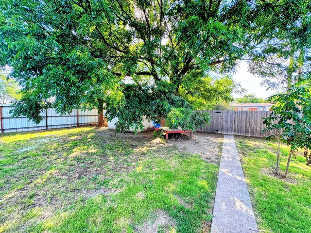 a view of a backyard with large trees and wooden fence