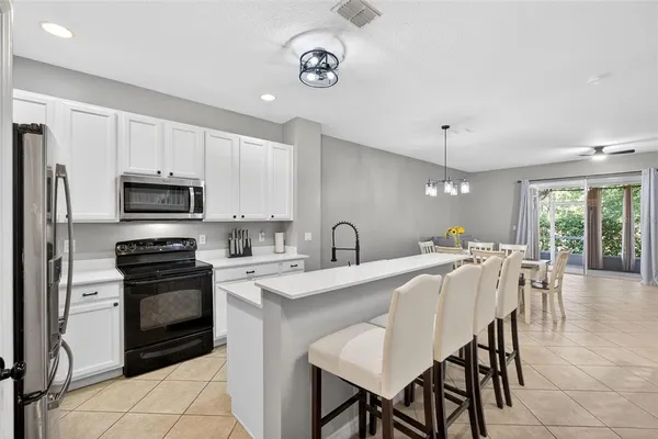 a kitchen with stainless steel appliances a stove a sink a microwave a refrigerator and white cabinets with wooden floor