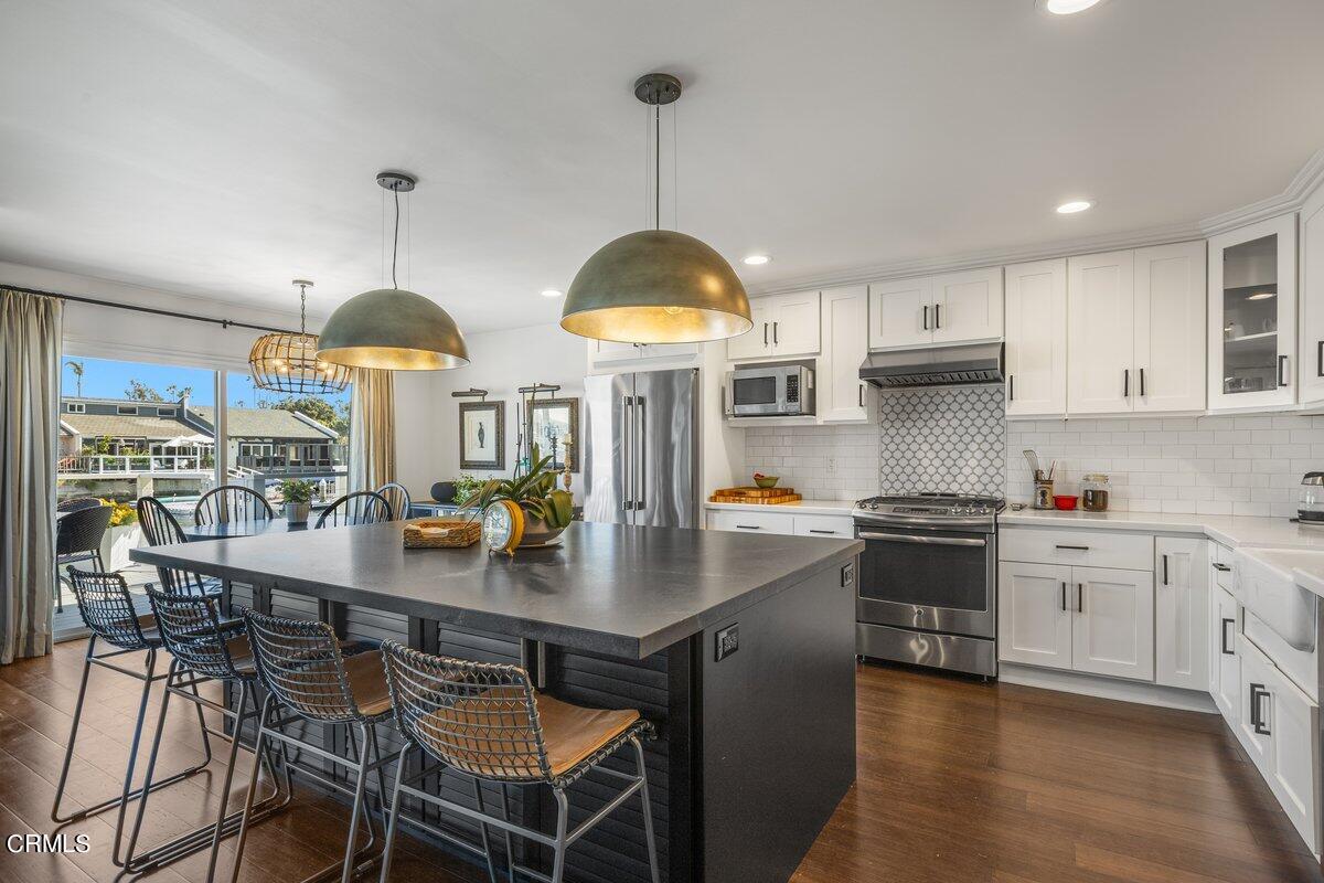 4612 Falkirk Bay Oxnard, CA 93035 - Photo 10 of 39 a kitchen with stainless steel appliances a stove a sink a dining table and chairs with wooden floor