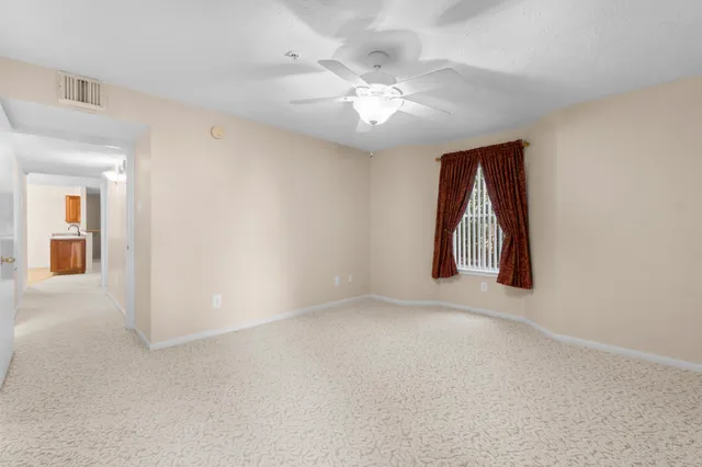 an empty room with chandelier fan and windows