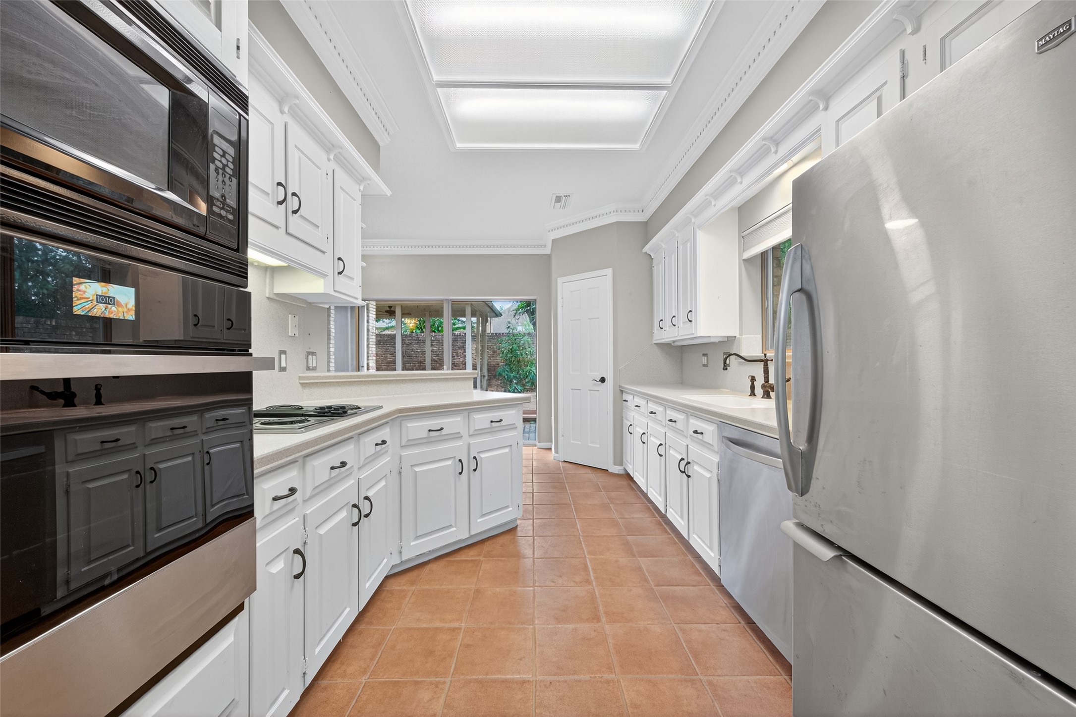 901 Longmire Road, Unit 13 Conroe, TX 77304 - Photo 24 of 46 Bright, spacious kitchen with modern stainless steel appliances, white cabinetry, and terracotta tile flooring. Large windows provide natural light and a view of the outdoor area.
