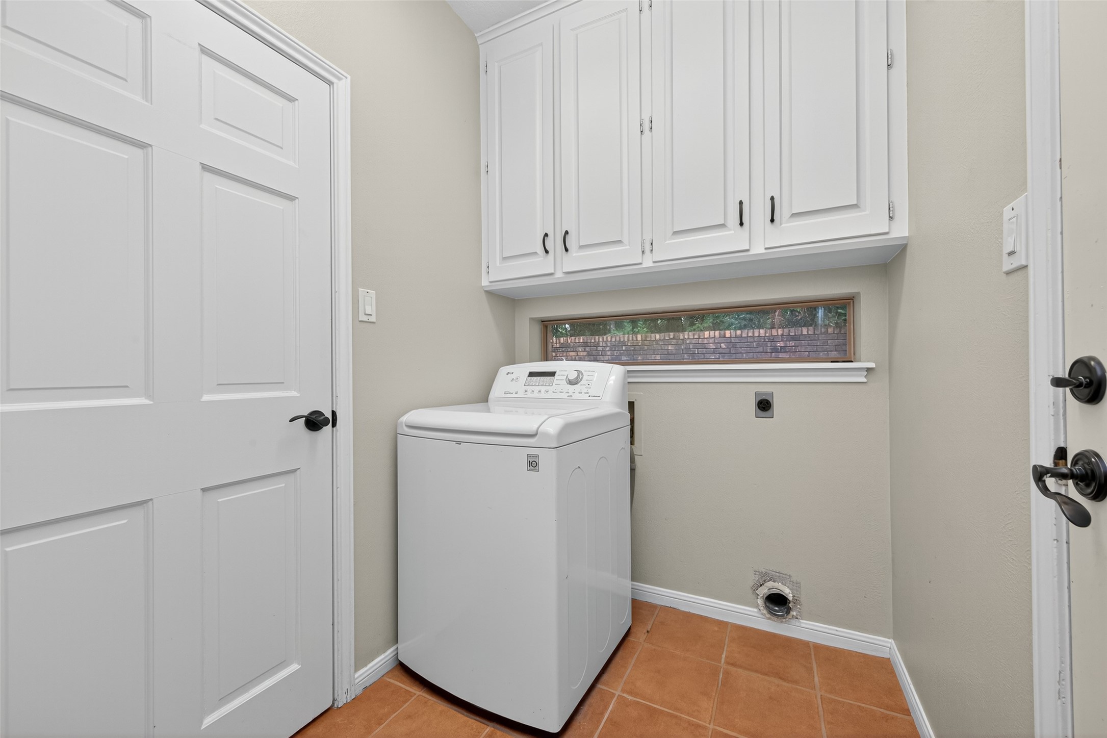 901 Longmire Road, Unit 13 Conroe, TX 77304 - Photo 26 of 46 This photo shows a compact laundry room featuring a top-loading washing machine, white cabinetry for storage, a small horizontal window for natural light, and terracotta tile flooring. Washer included.