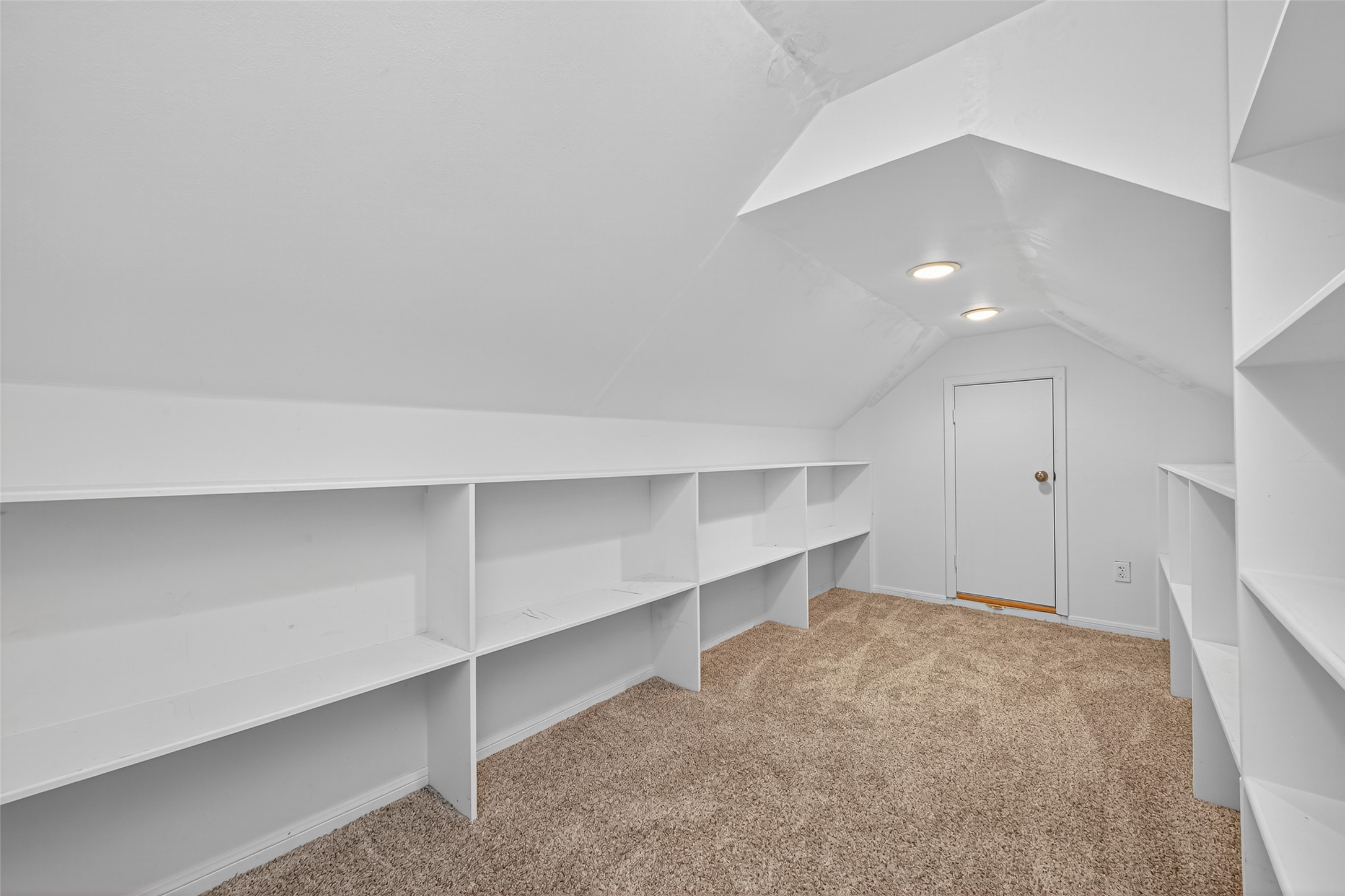 901 Longmire Road, Unit 13 Conroe, TX 77304 - Photo 43 of 46 This photo shows a cozy attic space with built-in shelving, ideal for storage or a small workspace. The room features a sloped ceiling, carpeted floor, and recessed lighting, creating a functional and inviting area.