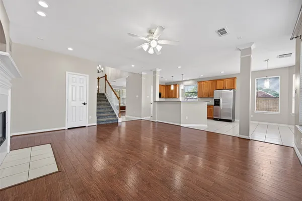 a view of an empty room with wooden floor a ceiling fan and kitchen view