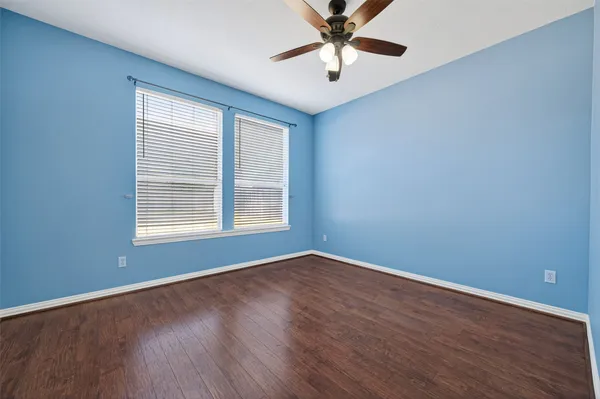 an empty room with wooden floor fan and windows