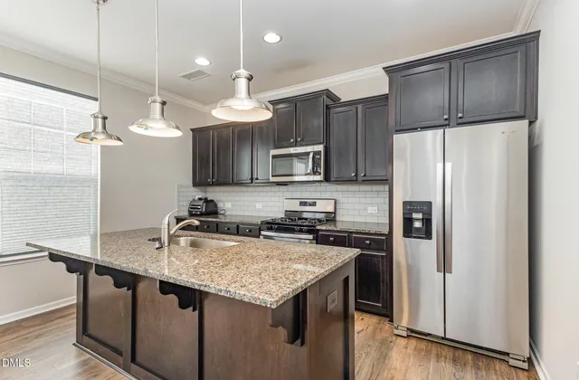 a kitchen with granite countertop a refrigerator a sink a stove a kitchen island and cabinets