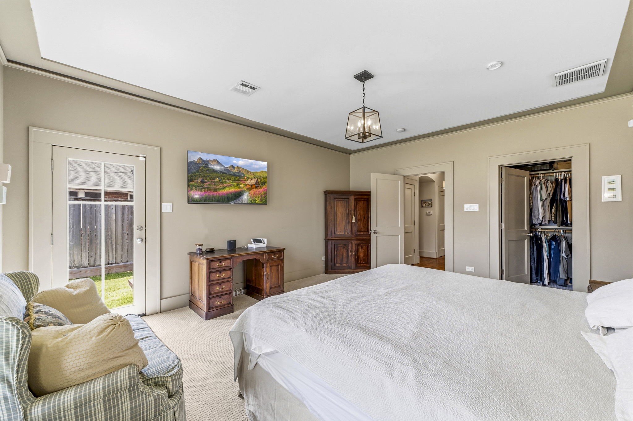 1521 Kipling Street Houston, TX 77006 - Photo 23 of 35 This spacious bedroom features a cozy atmosphere with neutral tones, a large bed, and ample natural light from the glass door leading outside. It includes a walk-in closet, a classic wooden desk, and stylish lighting.