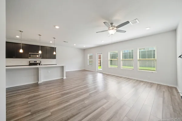 a view of an empty room with wooden floor and a kitchen