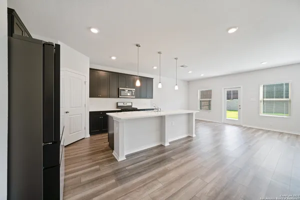 a large kitchen with kitchen island a sink dishwasher a refrigerator and white cabinets with wooden floor